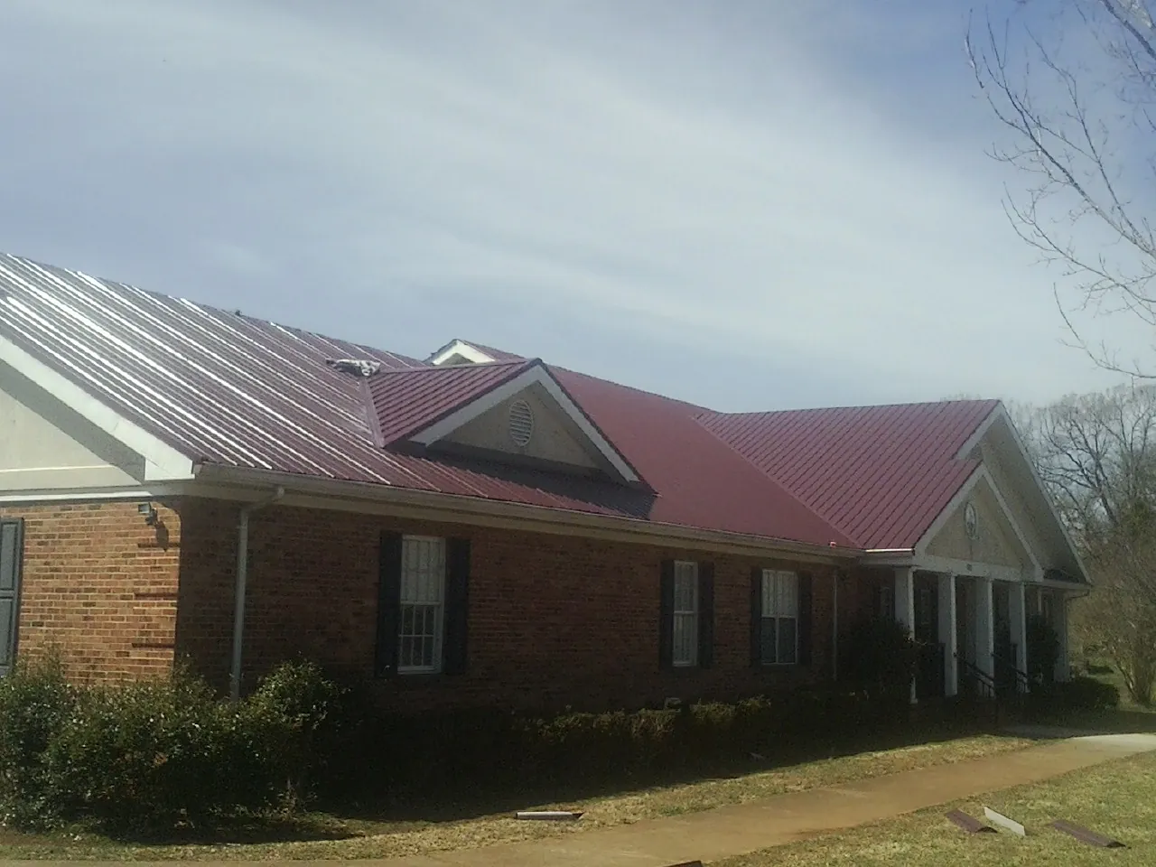 Red metal roof with gabled entries on a long brick building, from a Hail Damage Roof Repair job in Talbotton