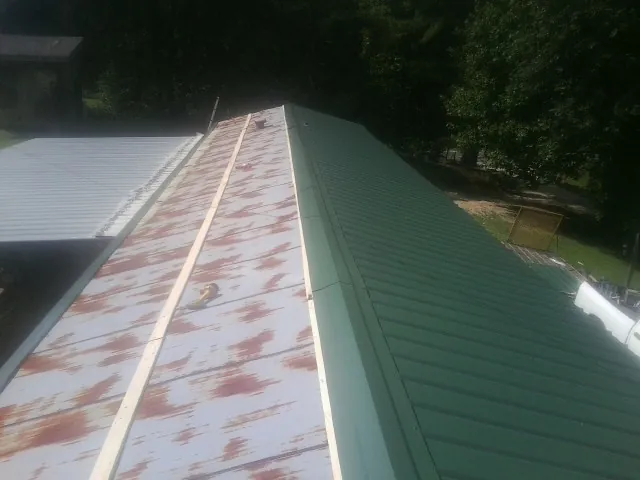 Old rusted panels beside newly installed green metal roofing — Wind Damage Roof Repair by Roofing Brothers in Talbotton