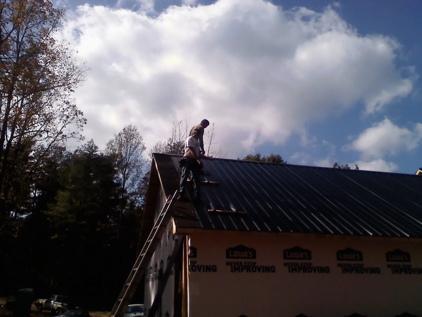 Roofer fastening dark metal panels high against a cloudy sky, from a Roof Inspection job in Talbotton