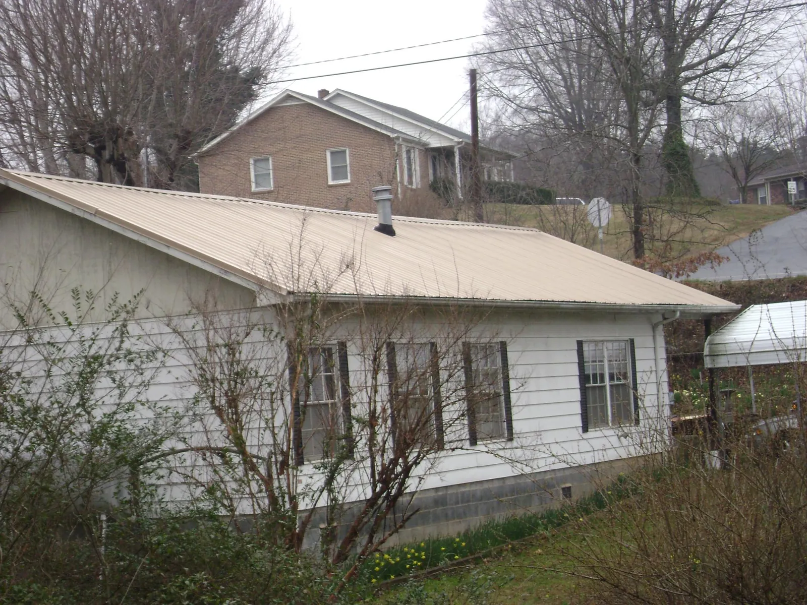 Tan metal roof on a white sided house set into a hillside — Commercial Roofing by Roofing Brothers in Talbotton